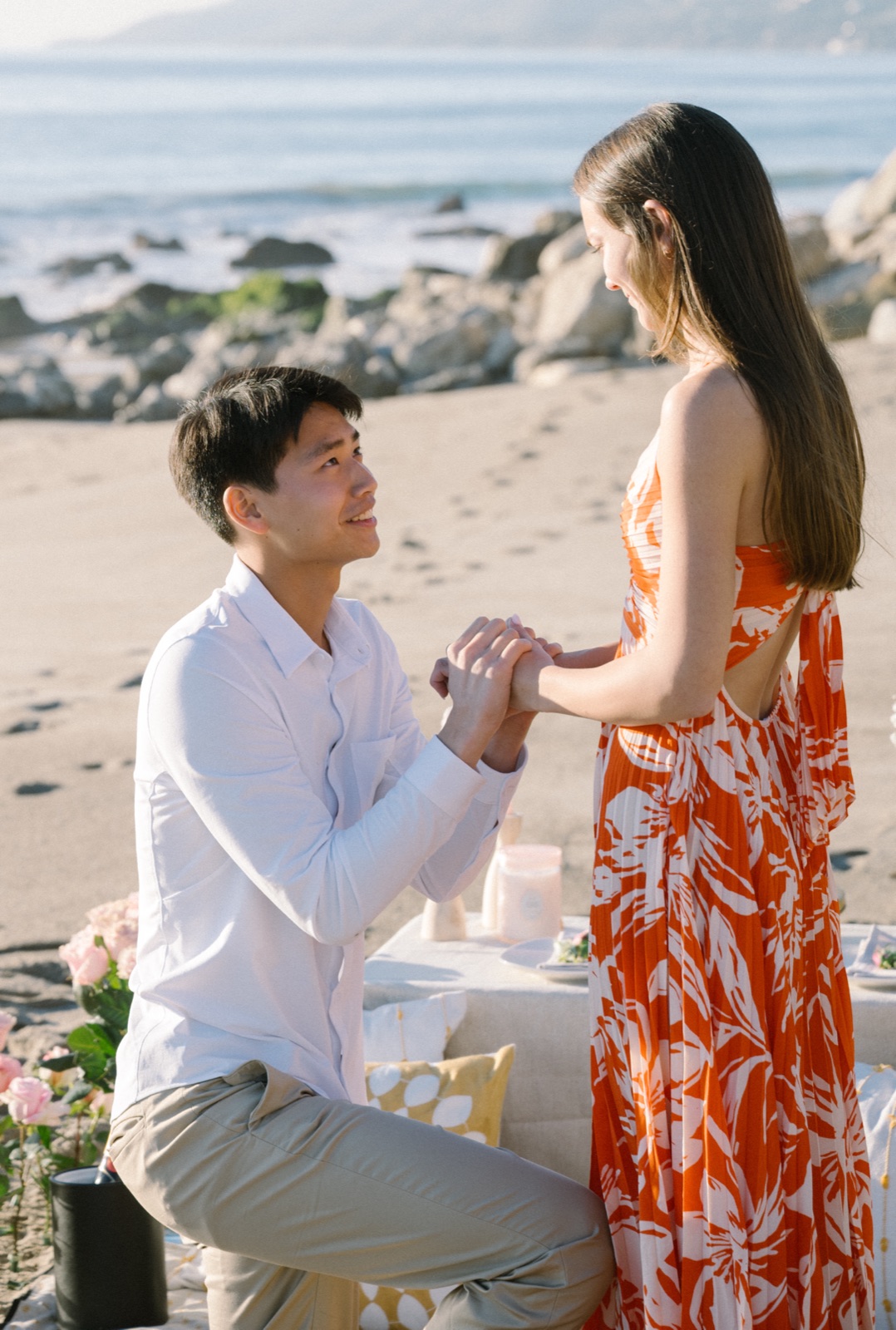 Jonathan on one knee holding Courtney's hands, both smiling, at Point Dume